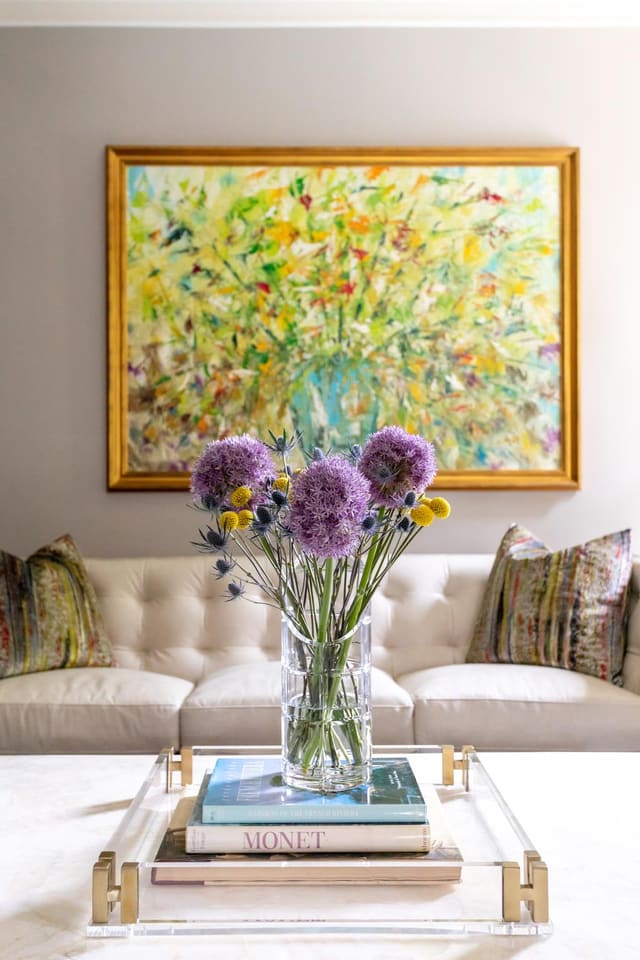 Beautiful John Richard painting above a white leather tufted sofa with fresh flowers sitting on the cocktail table.
