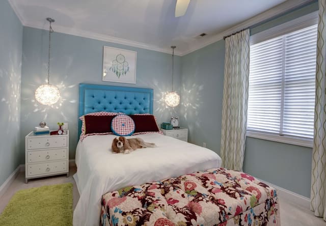 Cute girl's bedroom with pendant light fixtures, blue upholstered headboard, drapery panels, and colorful bench