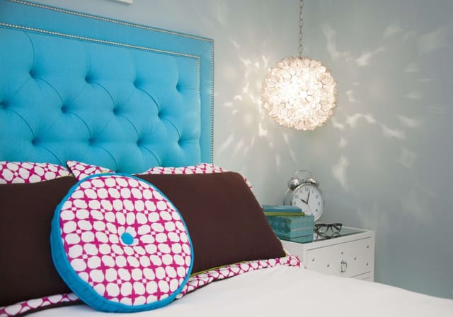 Upholstered, tufted, blue headboard with pink and blue accent pillows and fun pendant light