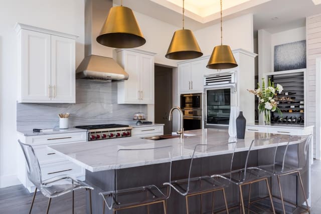 Kitchen of Apex Home featuring granite backsplash, brass pendants and acrylic barstools