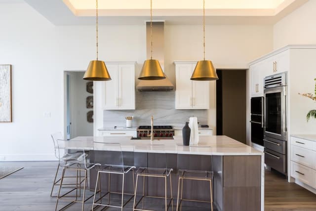 Kitchen of Apex Home featuring granite backsplash, brass pendants and acrylic barstools