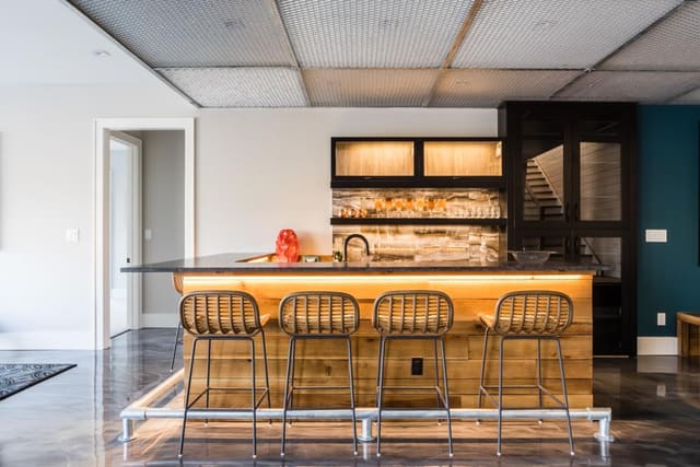 Basement Entertainment Room of Apex home with stained concrete flooring, under-lit bar and rattan barstools