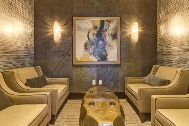 Parlor of Cary Bank featuring wallpaper, 4 chairs, bronze cocktail table, original artwork and quartz sconces.