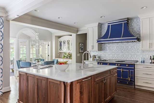 Kitchen with stained island with white countertops. custom blue range and hood, cream cabinets, and unique tile backsplash
