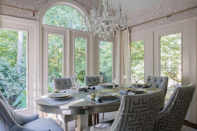 Cary Dining Room with Cherry Blossom wallpaper, cream chevron drapery panels on gold hardware, dining table with cream base and platinum top, and upholstered tufted dining chairs with greek key print backs and solid fronts