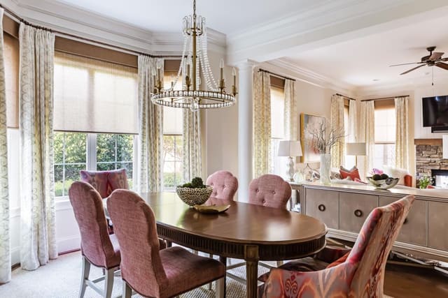 Open floorplan with Dining Room opening into Family Room.  Featuring window shades with neutral drapery panels, dining table with upholstered dining chairs and elegant light fixture.