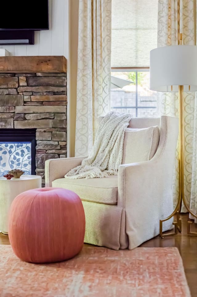 Close-up of cozy cream chair with coral pouf ottoman and brass floor lamp.