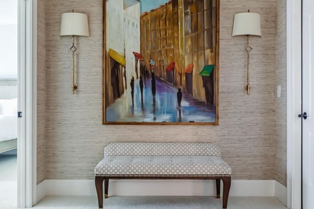 Landing featuring grasscloth wallpaper, bench, brass sconces and original artwork.