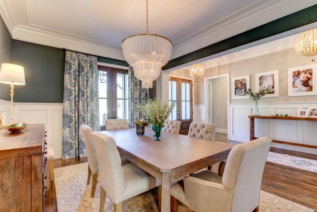 Dining Room with Teal walls, beaded chandelier, upholstered dining chairs, gold mirror, custom window treatments, and neutral patterned rug