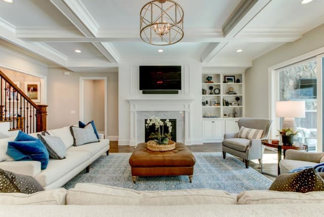 Family room in Chapel Hill custom home with blue area rug, leather ottoman, 2 sofas, pair of chairs, and accessorized built-ins