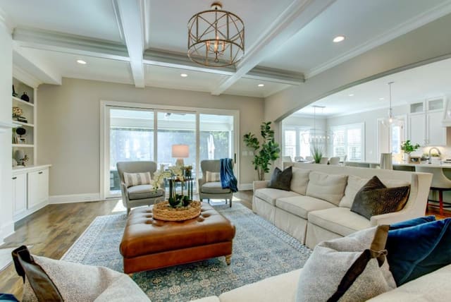 Family room in Chapel Hill custom home with blue area rug, leather ottoman, 2 sofas with contrast throw pillows, pair of chairs, looking into Kitchen