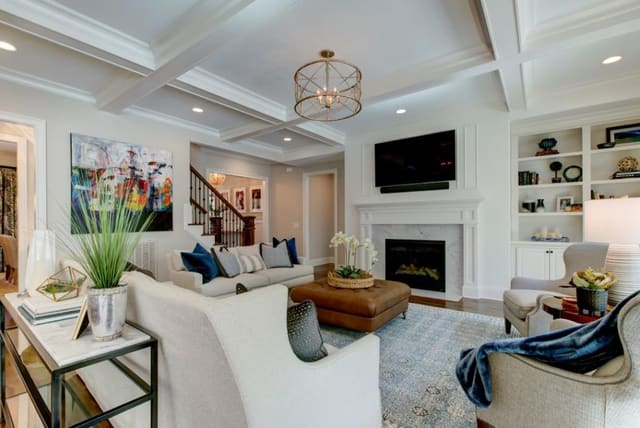 Family room in Chapel Hill custom home with blue area rug, leather ottoman, 2 sofas, pair of chairs, and accessorized built-ins