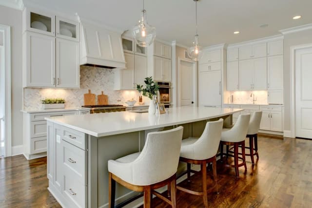 Kitchen in Chapel Hill custom home with white cabinets and range hood, contrast grey island, white barstools, hanging pendants and lantern over breakfast table