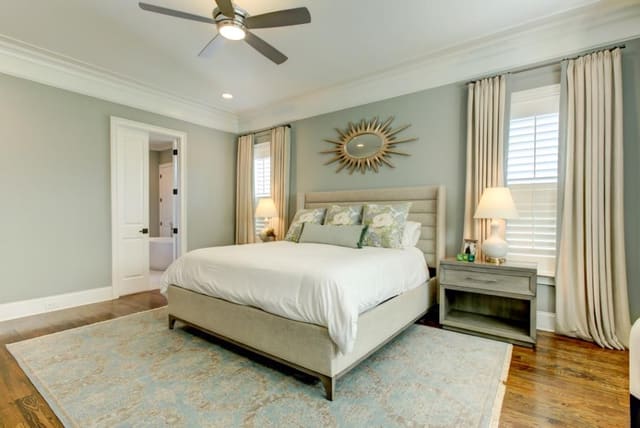 Master Bedroom in Chapel Hill home with aqua walls and area rug, upholstered bed, starburst mirror, pair of white lamps, and custom neutral window treatments with aqua fabric band down lead edge