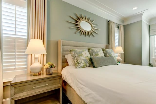 Master Bedroom in Chapel Hill home with aqua walls, upholstered bed with custom pillows, starburst mirror, pair of white lamps, and custom neutral window treatments with aqua fabric band down lead edge