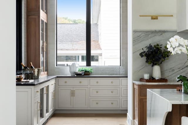 Kitchen showcasing marble waterfall countertops and white cabinetry with gold hardware