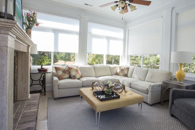 Sun Room with silhouette shades, custom sectional with contrasting throw pillows, ottoman with acrylic legs, leather wrapped side table, yellow lamp, and sisal area rug.