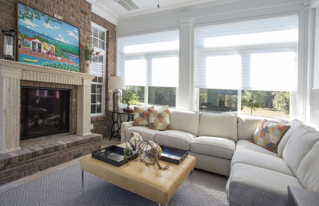 Sun Room with silhouette shades, custom sectional with contrasting throw pillows, ottoman with acrylic legs, and sisal area rug.