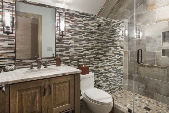Remodeled bathroom with full tile wall and smooth stone shower floor.