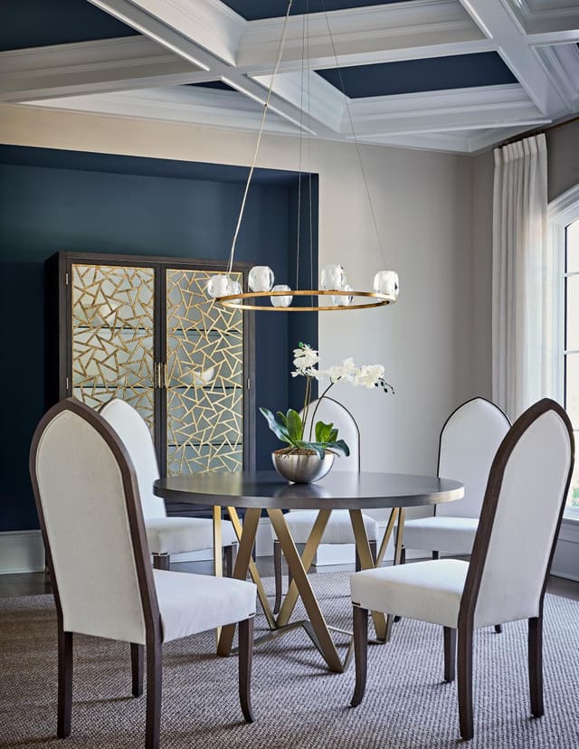 Dining Room of Wake Forest home featuring coffered ceiling, abstract china cabinet, table with gold base and modern gothic chairs