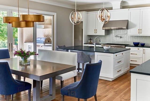 Kitchen of Wake Forest Home with blue upholstered dining chairs, gold and white pendant lights, and white cabinets with gold hardware.