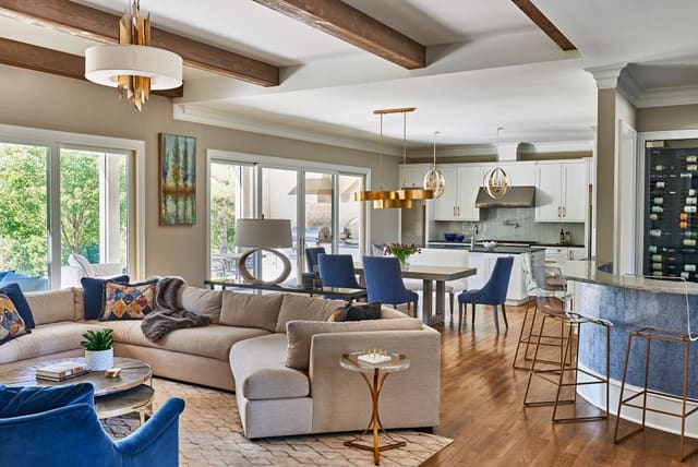 Family Room in Wake Forest home with open floor plan and exposed beams, featuring relaxed sectional, lucite barstools, and blue chairs