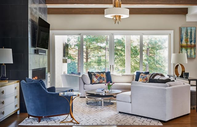 Family Room in Wake Forest home with exposed beams, horizontal fireplace, colorful artwork, blue velvet chair, twin ivory and gold chests, and relaxed sectional.