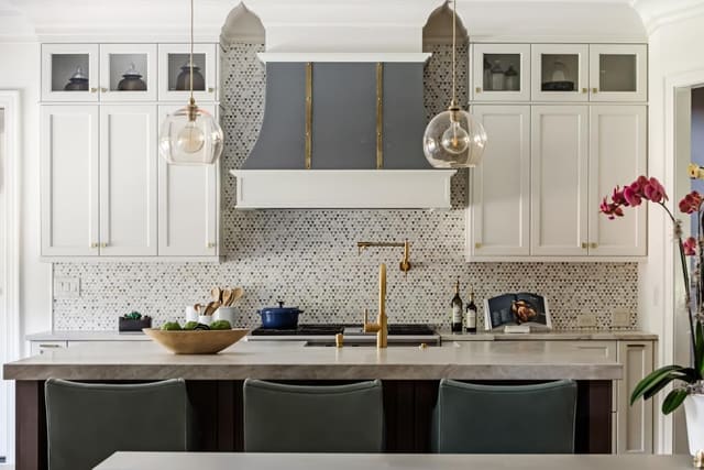 Kitchen showing clear glass pendants, grey leather barshools, beautiful mosaic tile and custom metal range hood.