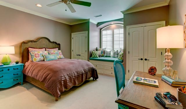 Girls bedroom with custom bedding, blue accent furniture, and custom window seat with pillows