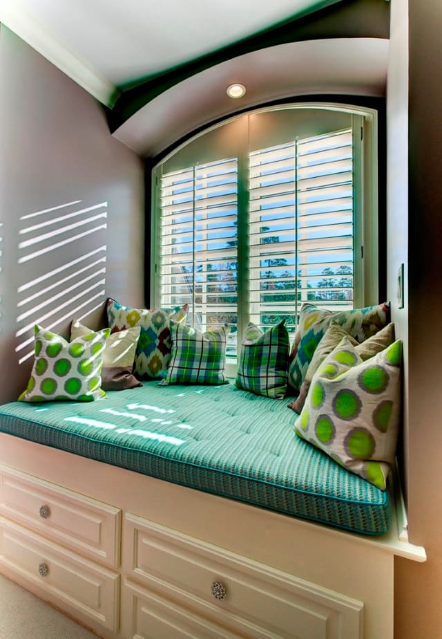 Girls bedroom with custom window seat with bright pillows and arched shutter