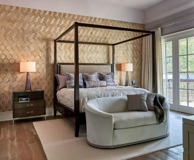 Bedroom with lavendar walls, wallpapered accent wall, fuzzy rug, four poster bed, velvet sofa, and custom pillows and window treatments.