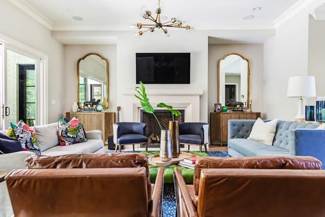 Looking into N. Raleigh Family Room with brown leather chairs, 2 sofas, chiang mai throw pillows, funky light fixture and twin mirrors and chest.