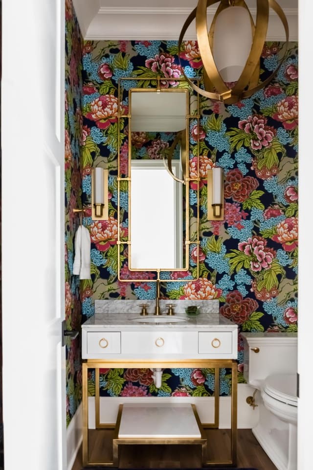 Powder Room with bright patterned wallpaper, brass hanging pendant, white marble vanity with brass accents and brass sconces and mirror.