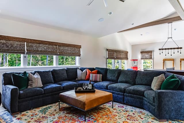 N. Raleigh Game Room with blue accent wall, woven wood shades, colorful rug, leather ottomanand blue sectional