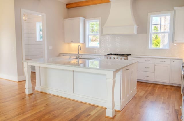 Kitchen in North Raleigh home with exposed wood beams, white cabinets, white range hood, and large island with white quartz countertop.