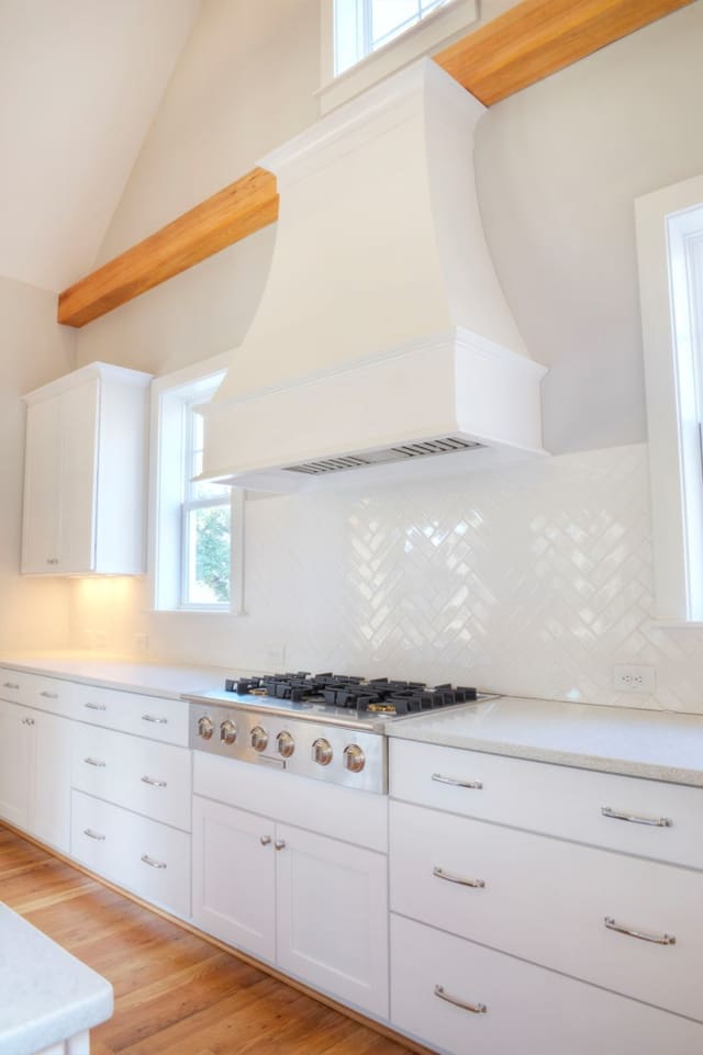 Kitchen in North Raleigh home with exposed wood beams, white cabinets, white range hood, and white backsplash.