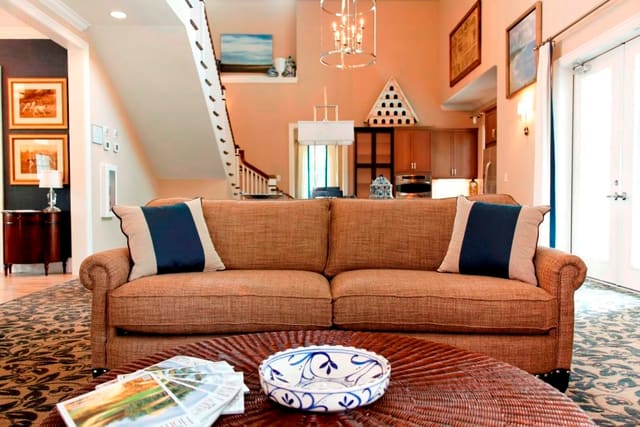Gathering Room in clubhouse with wicker coffee table, sofa with contrasting throw pillows, and leather chairs on navy and tan carpet