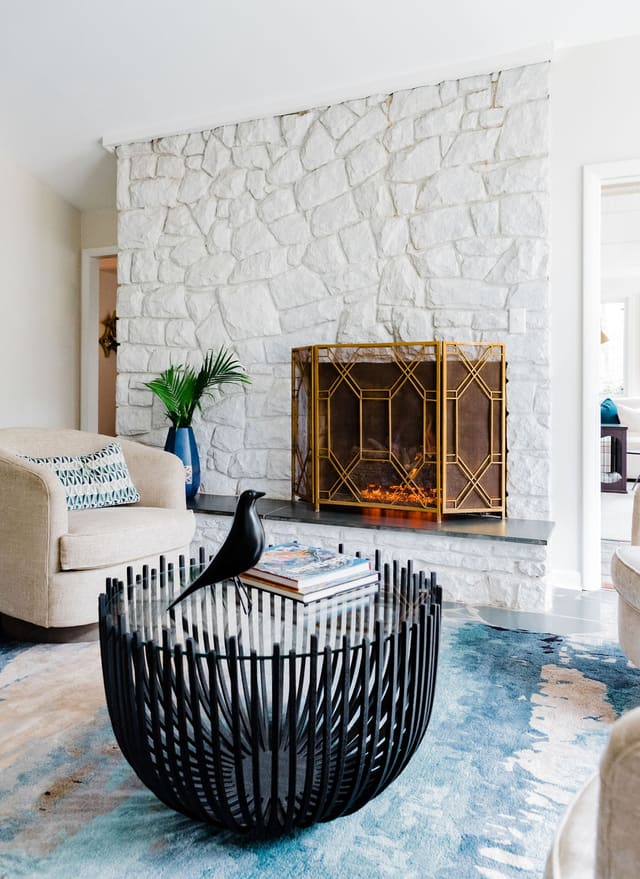 Close up of blackened steel coffee table showing painted stone fireplace in the background with brass fireplace screen.