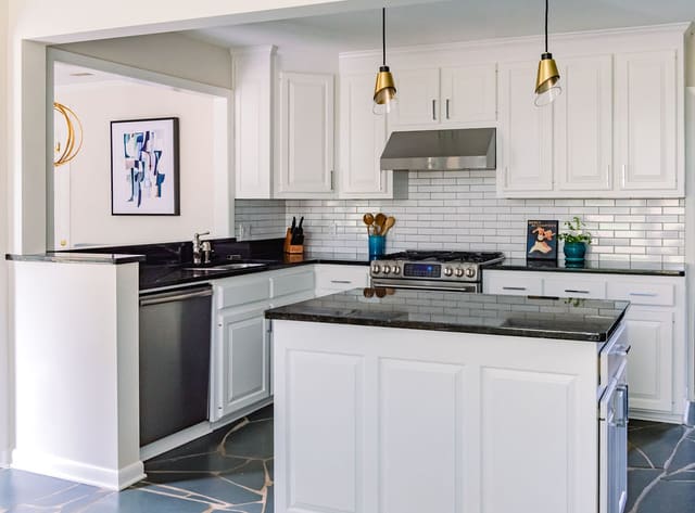 Remodeled Kitchen with white cabinets, dark countertops, white tile backsplash and brass pendants