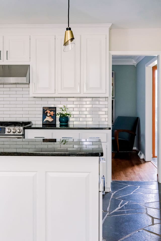 Remodeled Kitchen with original slate flooring, white cabinets, dark countertops, white tile backsplash and brass pendants