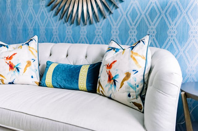 Close up of tufted back settee with gorgeous throws on teal wallpapered accent wall.