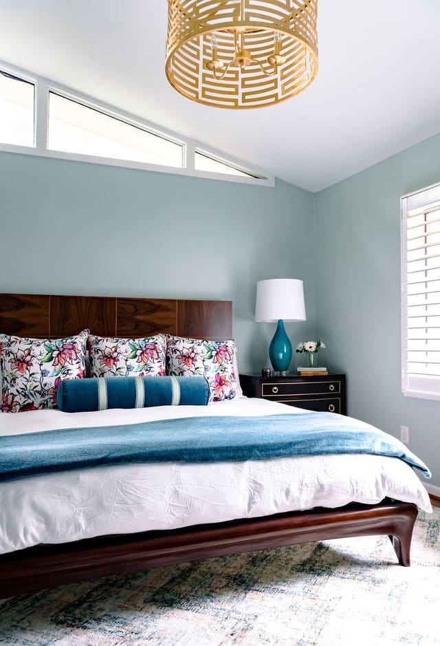 Master Bedroom with gold drum light, mahogany bed, nightstand with gold striping, cozy area rug and custom bedding.