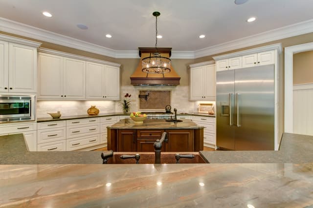 Raleigh Kitchen with two types of granite on island, white cabinets, chandelier, and custom range hood