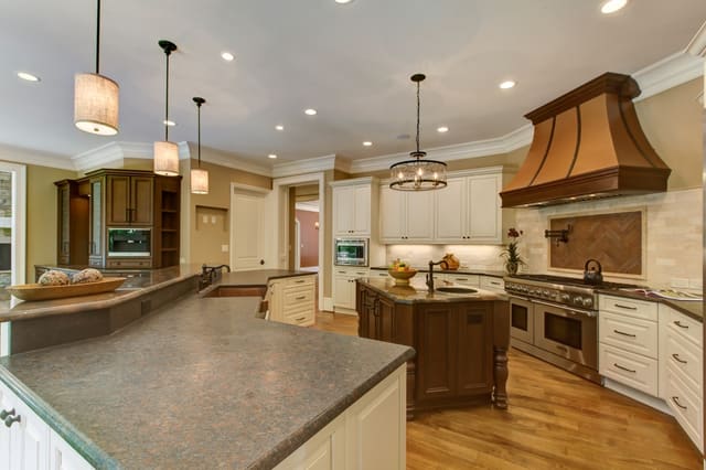 Raleigh Kitchen with two types of granite on island, smaller island with prep sink, white cabinets, chandelier, and custom range hood