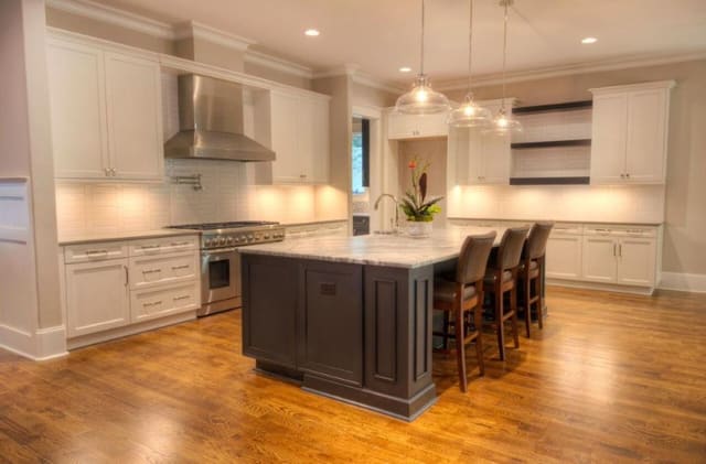 Kitchen in new Raleigh Home with white cabinets, white tile backsplash, gray island, and granite countertops.