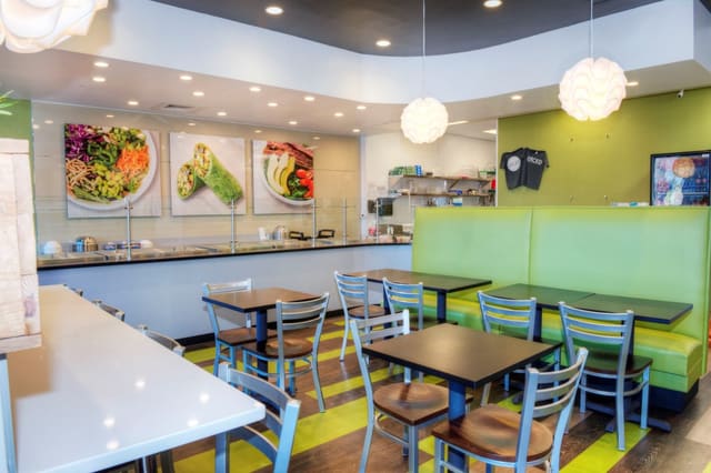 Interior of Diced Restaurant in Raleigh with mixed color LVT flooring, green banquettes, black tables, silver chairs, and pendant lighting