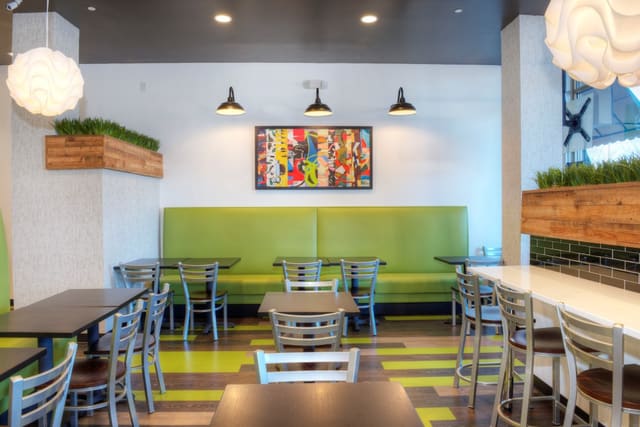 Interior of Diced Restaurant in Raleigh with mixed color LVT flooring, colorful artwork, green banquettes, black tables, silver chairs, and pendant lighting