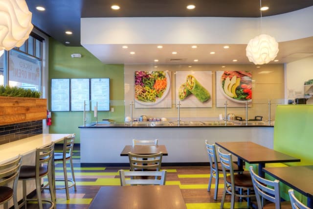 Interior of Diced Restaurant in Raleigh with mixed color LVT flooring, green banquettes, black tables, silver chairs, and pendant lighting