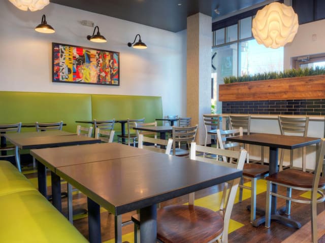 Interior of Diced Restaurant in Raleigh with mixed color LVT flooring, colorful artwork, green banquettes, black tables, silver chairs, and pendant lighting