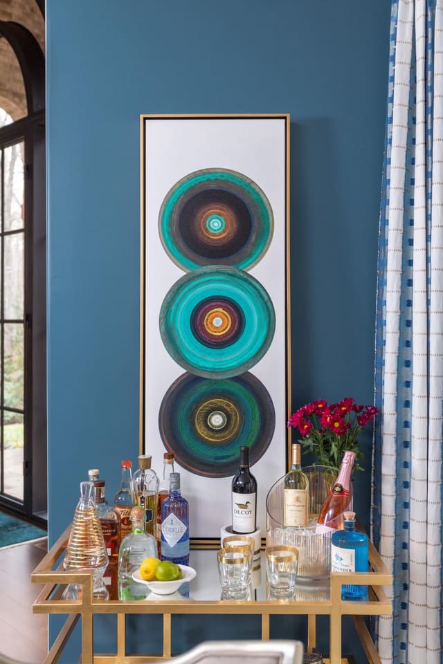 Framed circle art overtop of a filled gold bar cart with fresh flowers.
